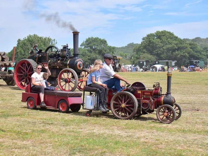 Nellie hauling a trailer full of passengers around the main ring at a steam rally, passing a full-size traction engine