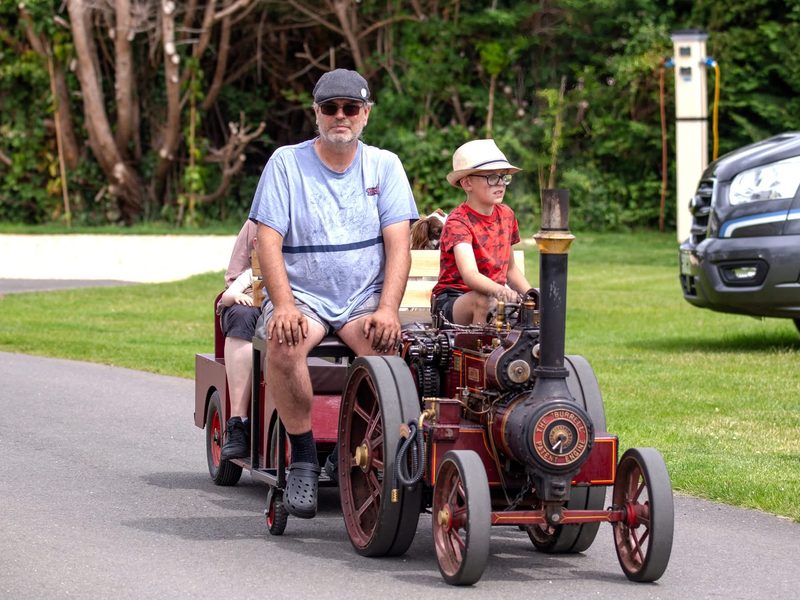 A young driver at Nellie's controls on a road run, with passengers riding on the trailer behind